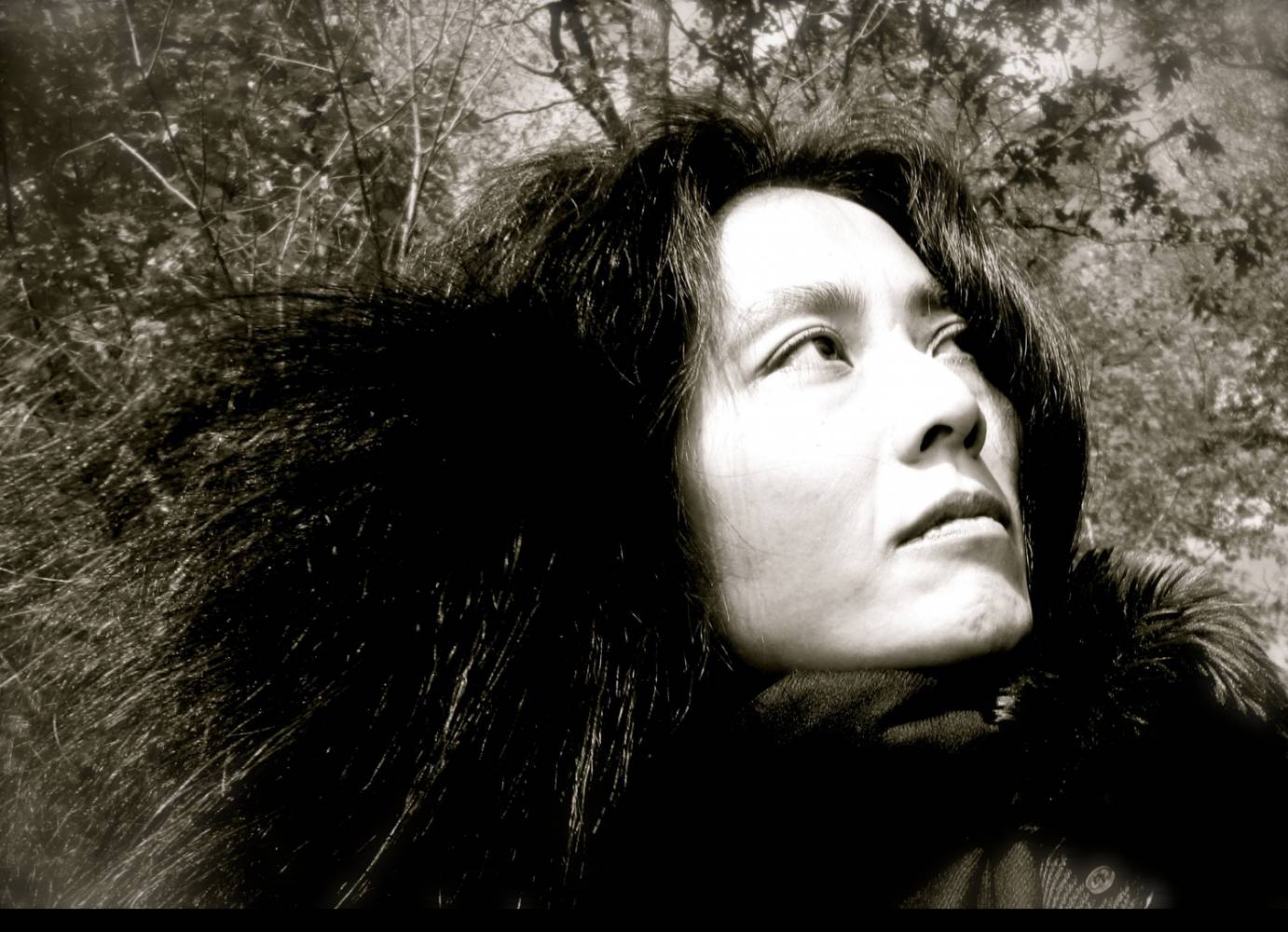 a black and white portraite of Mana Hashimoto outside in the daytime,among leaves, in a forest type setting. She faces on a high diagonal, and her hair seems wild like the twigs and branches around her